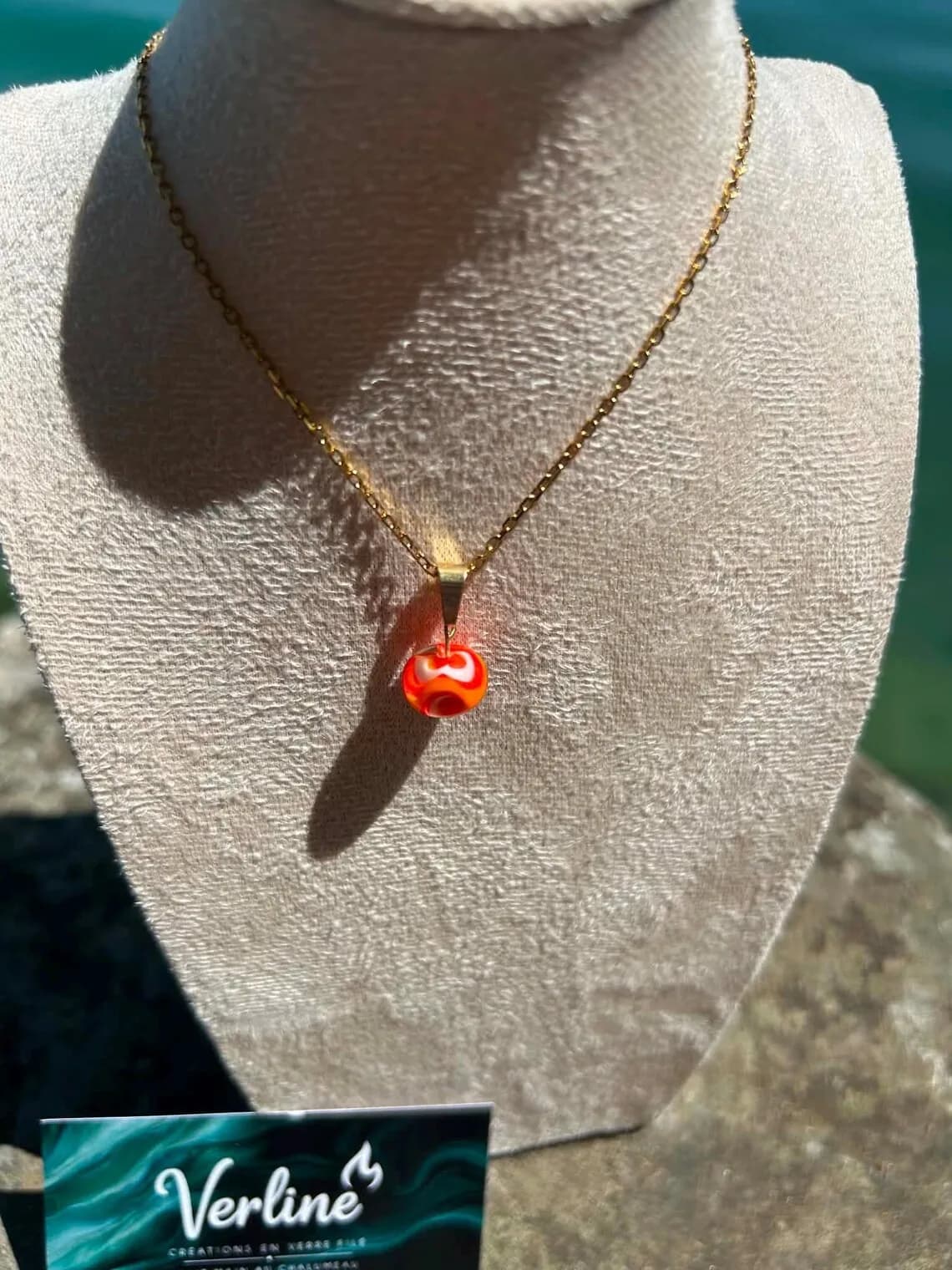 Gros plan de la perle en verre filé orange et rougeoyante montée sur une fine chaîne dorée.