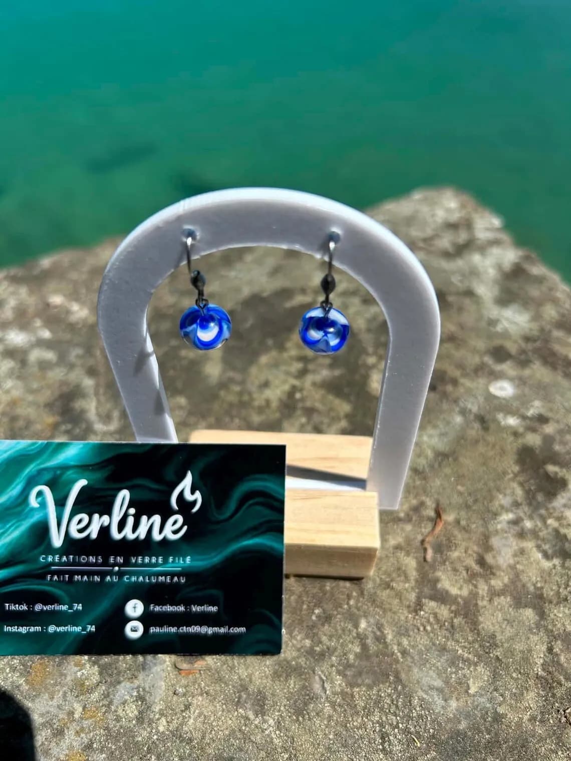 Vue en plongée des boucles d'oreilles Océane aux motifs bleus et blancs posées sur un muret en pierre.