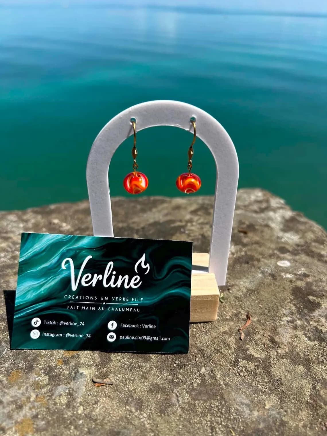 Vue de trois-quarts des boucles d'oreilles orange et dorées sur support blanc devant un fond marin.