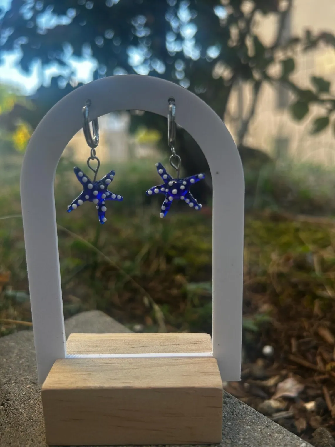 Paire de boucles d'oreilles étoiles de mer bleues en verre suspendues sur un support blanc.