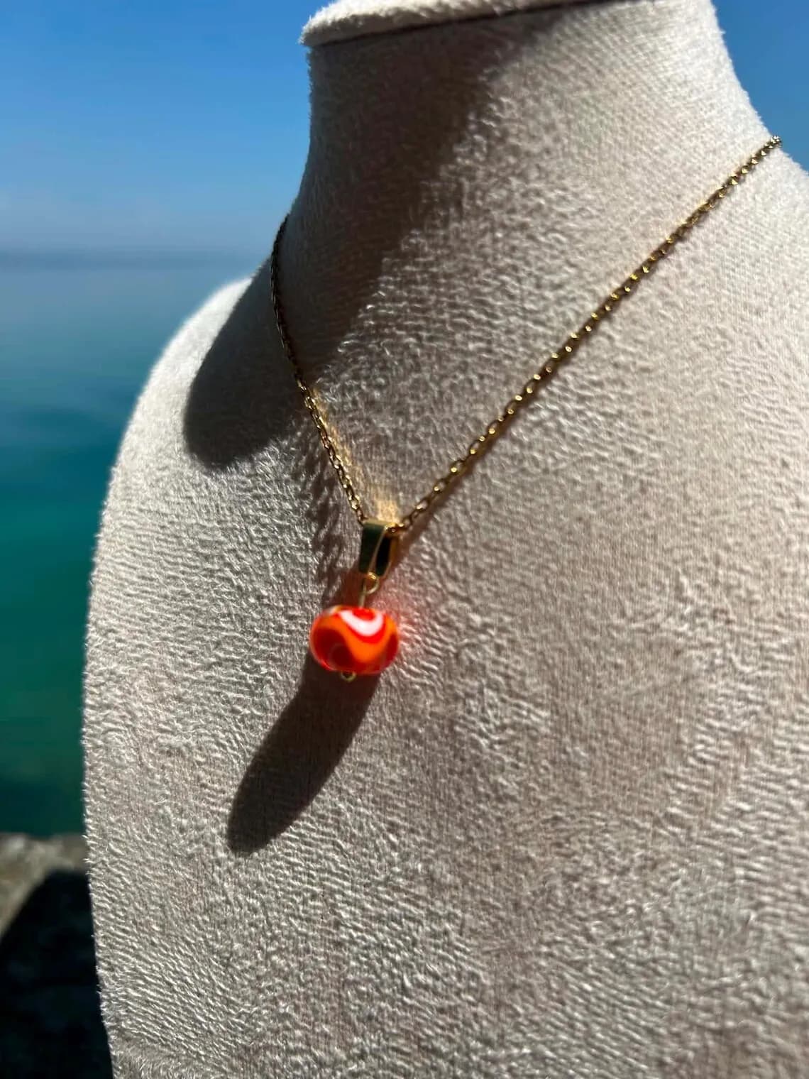 Gros plan sur le pendentif rond en verre filé aux nuances orangées monté sur chaîne dorée