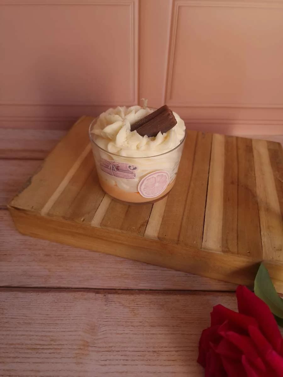 Bougie gourmande en verre avec dessus effet chantilly et bâtons de cannelle sur socle en bois