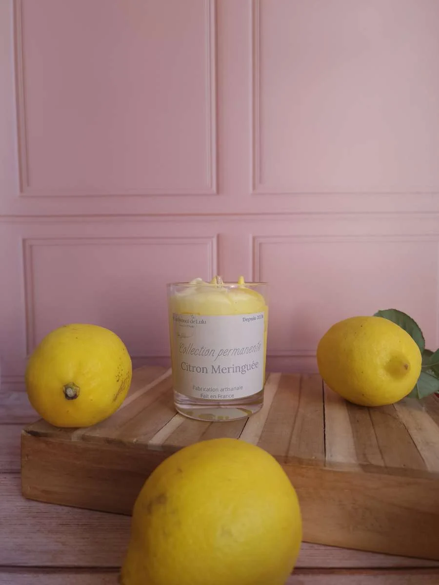 Bougie parfumée en verre aux nuances jaunes et blanches, entourée de citrons frais sur socle en bois.