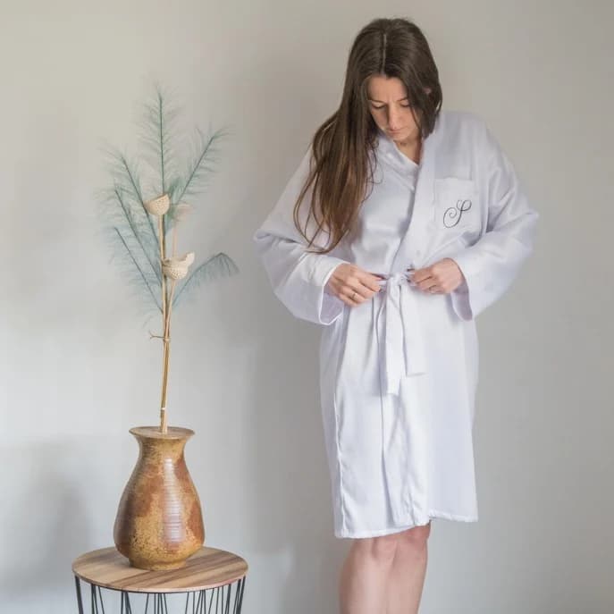 Femme assise sur un canapé vêtue du peignoir en satin blanc avec ceinture ajustée.
