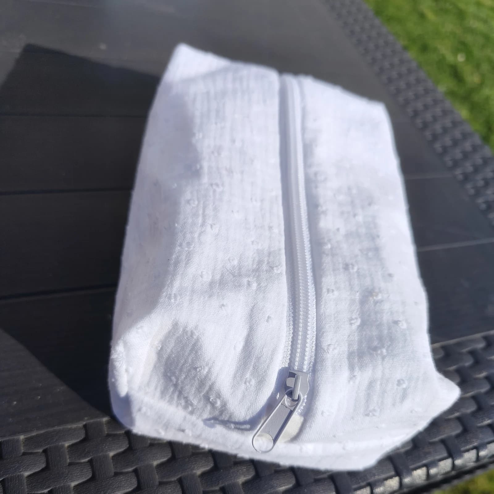 Trousse rectangulaire blanche en tissu souple à petits reliefs avec fermeture éclair blanche.