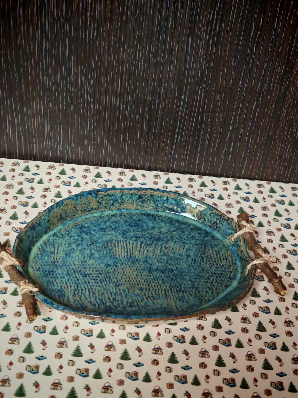 Plat ovale en céramique émaillée bleue vu du dessus, avec deux anses en bois attachées par des cordelettes.