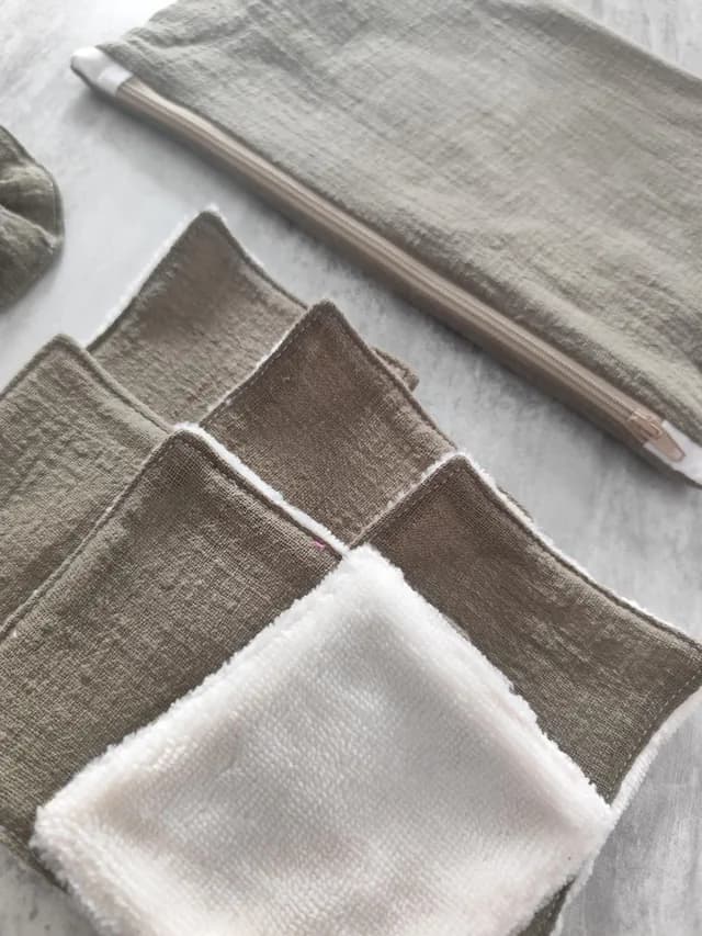 Gros plan sur les lingettes lavables douces taupe et blanche à côté de la pochette zippée assortie.
