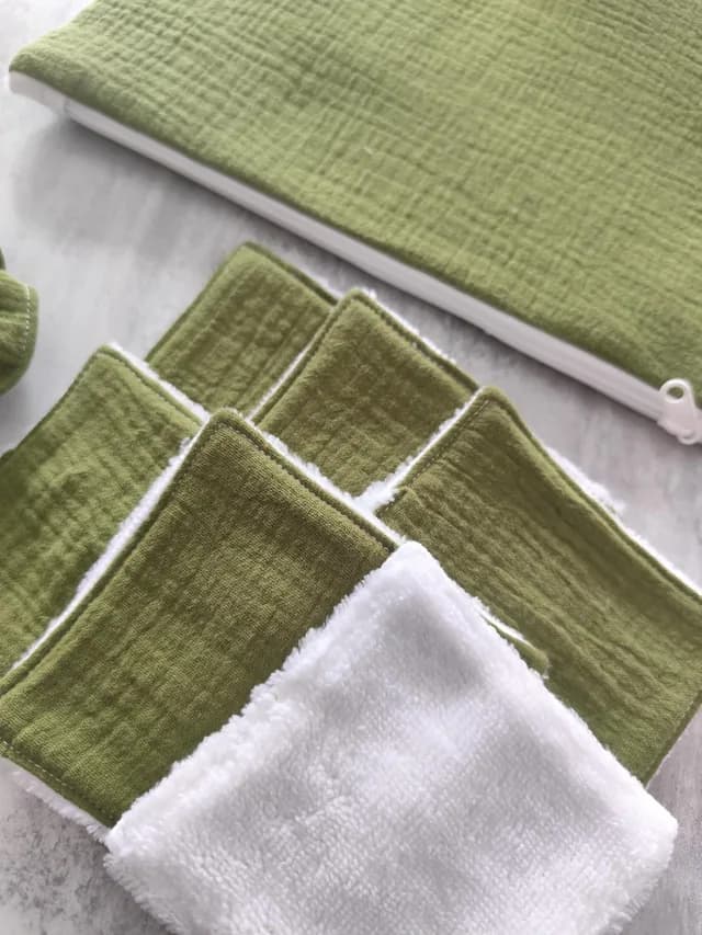 Détail des lingettes carrées lavables vert olive et blanches empilées près de la pochette zippée.