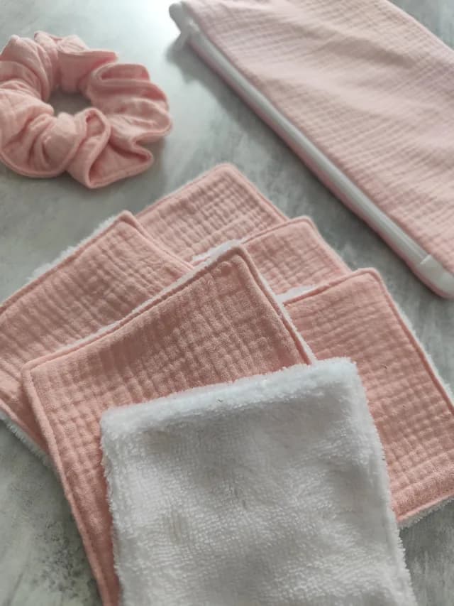 Vue rapprochée des lingettes lavables douces roses et blanche avec le chouchou et la pochette en fond.