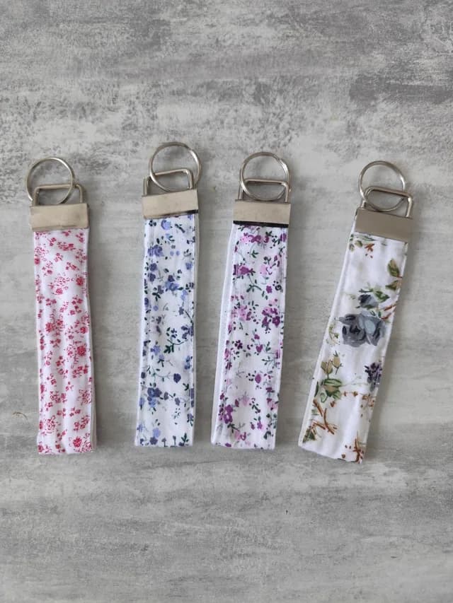 Quatre porte-clés ruban en tissu à motifs floraux rouge, bleu, violet et beige avec anneaux métalliques.