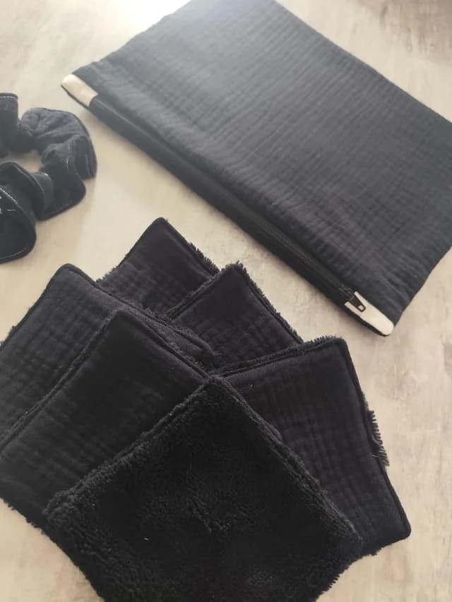 Vue rapprochée des lingettes lavables noires empilées avec la pochette et le chouchou coordonnés.