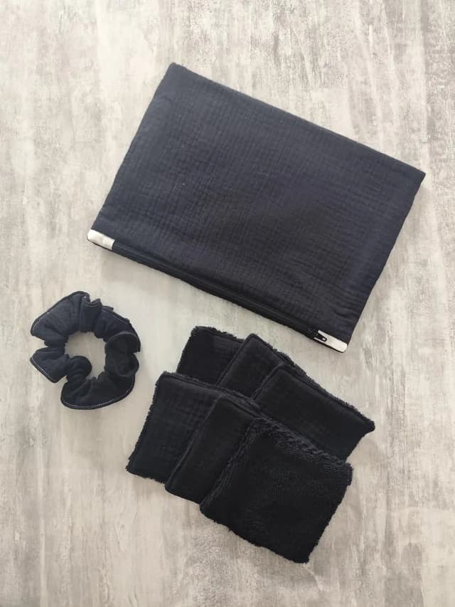 Pochette zippée noire, chouchou assorti et lingettes lavables carrées noires sur fond texturé.