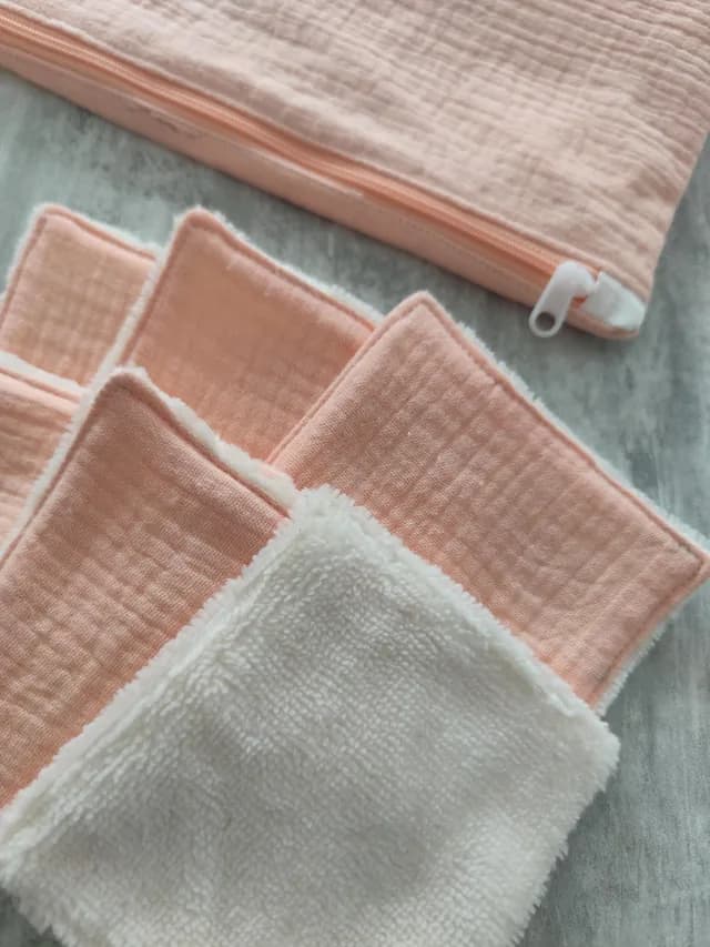 Détail des lingettes lavables roses et blanches empilées à côté de la pochette zippée.