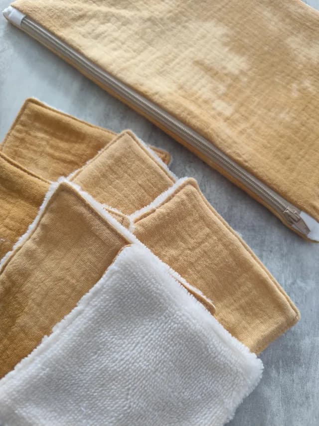 Gros plan sur les lingettes lavables douces blanches et jaune moutarde à côté de la trousse zippée.