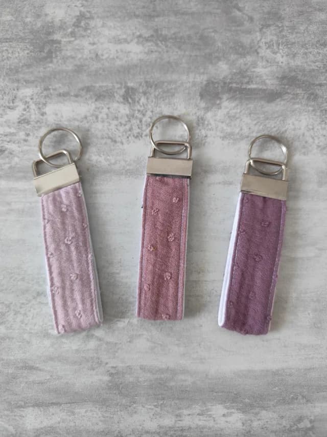 Trois porte-clés dragonnes en tissu rose pâle, rose poudré et violet à motifs en relief et attaches métalliques