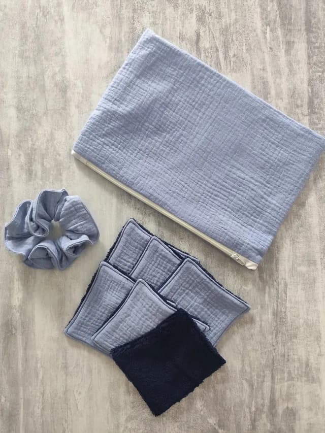Kit beauté avec pochette zippée bleue, chouchou assorti et lingettes lavables carrées sur fond marbré.