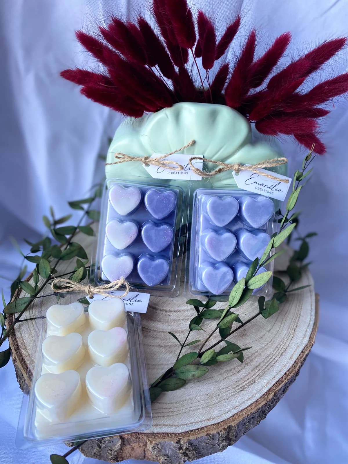 Tablettes clamshells de cire parfumée en forme de cœurs violets et blancs posées sur un rondin de bois décoré.