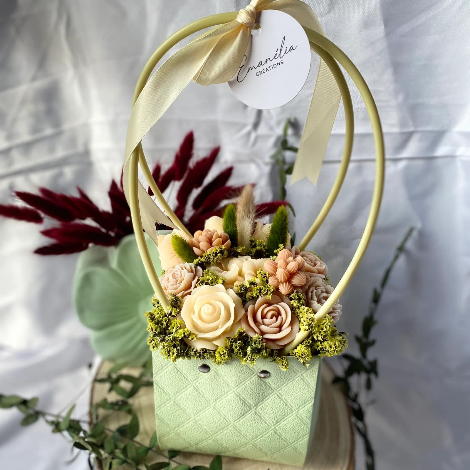 Panier vert clair garni de fleurs sculptées en cire tons beige et café avec des fleurs séchées et anse à ruban.