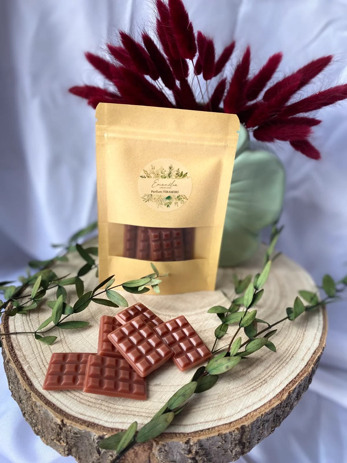 Sachet kraft et fondants marron en forme de tablette de chocolat posés sur un rondin de bois décoré.