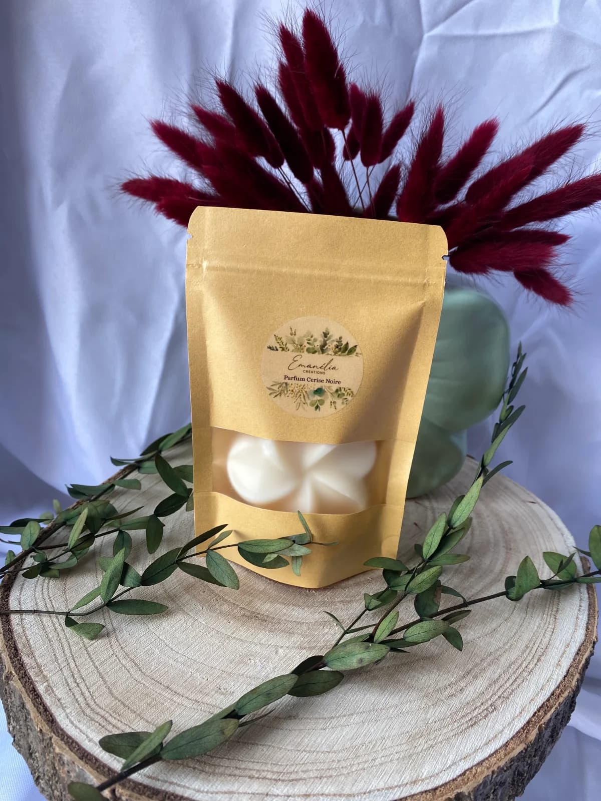 Sachet kraft avec fenêtre laissant voir un fondant blanc en forme de fleur sur un socle en bois.