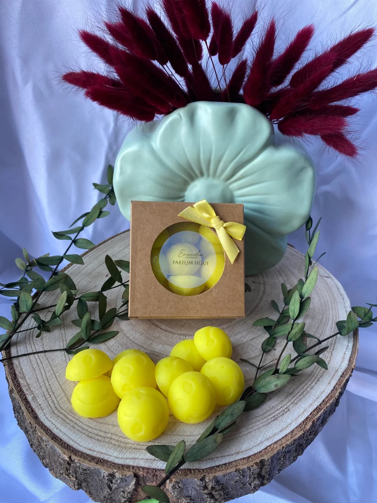 Boîte kraft et fondants smiley jaunes parfum figue présentés sur un rondin de bois décoré de feuillage.