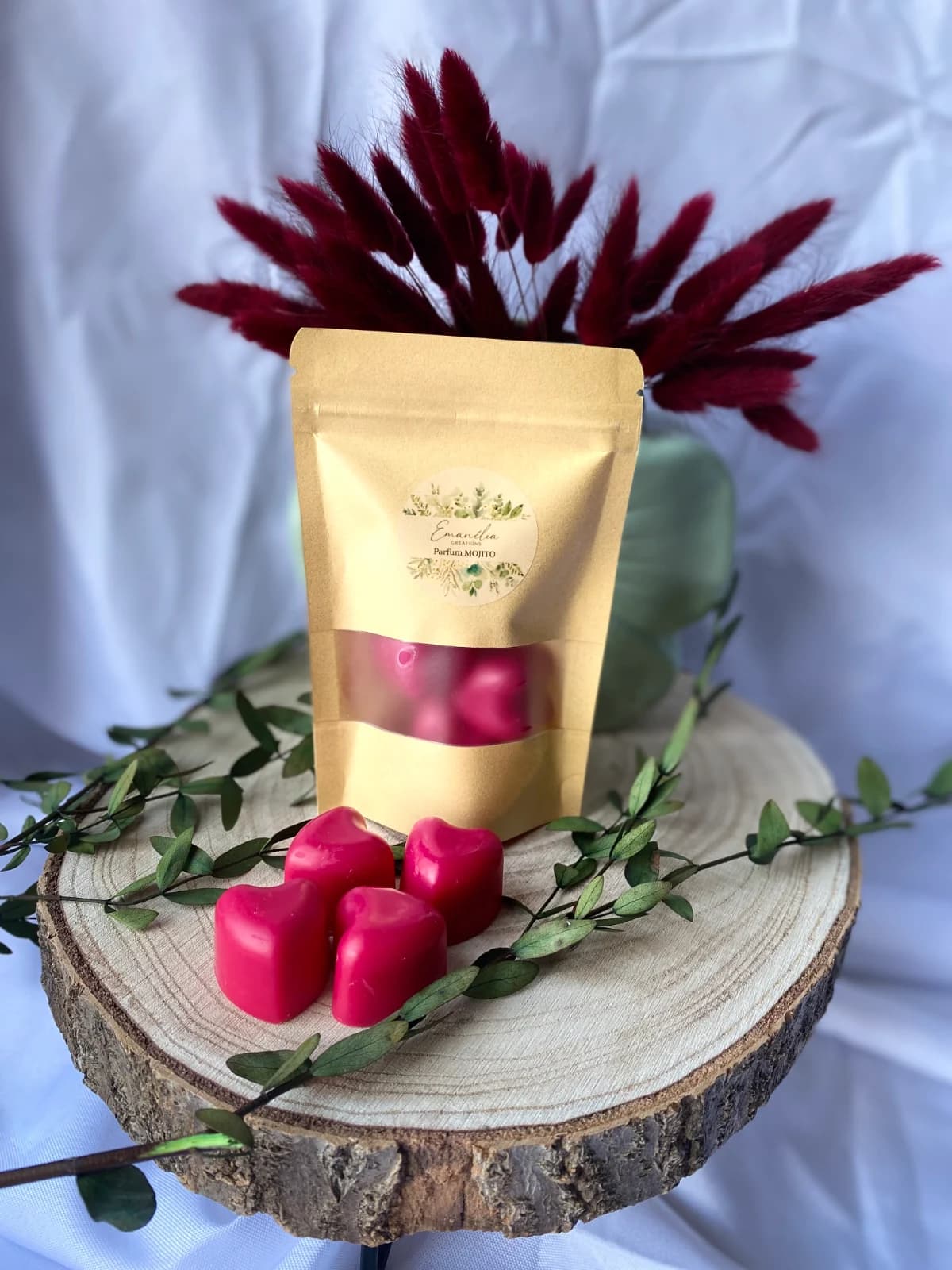 Sachet kraft et quatre fondants roses en forme de cœur posés sur une rondelle de bois avec végétaux.