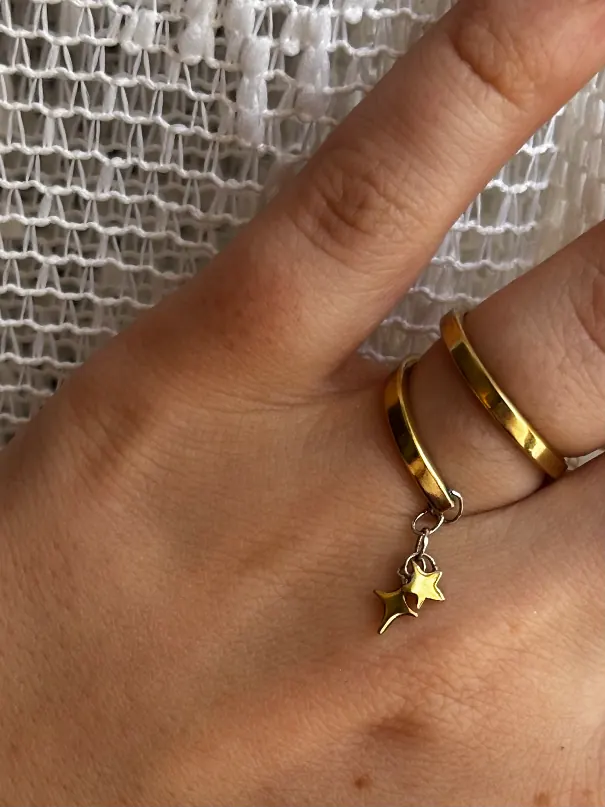Bague double anneau doré portée à la main avec deux petites étoiles pendantes