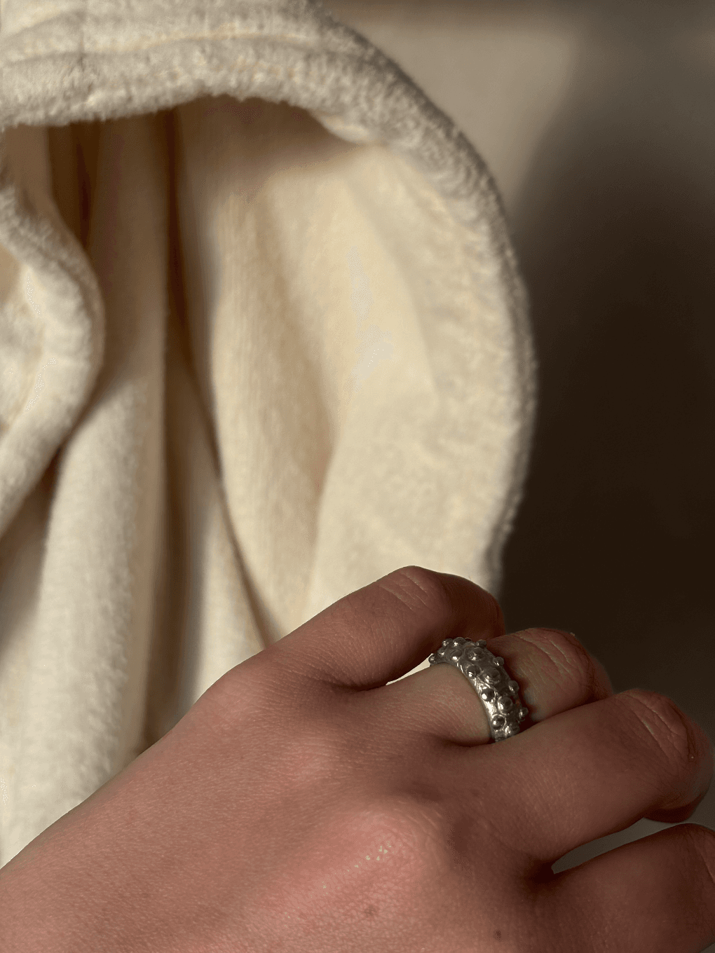 Gros plan sur la bague artisanale aux motifs de bulles portée au doigt sur fond de tissu clair.